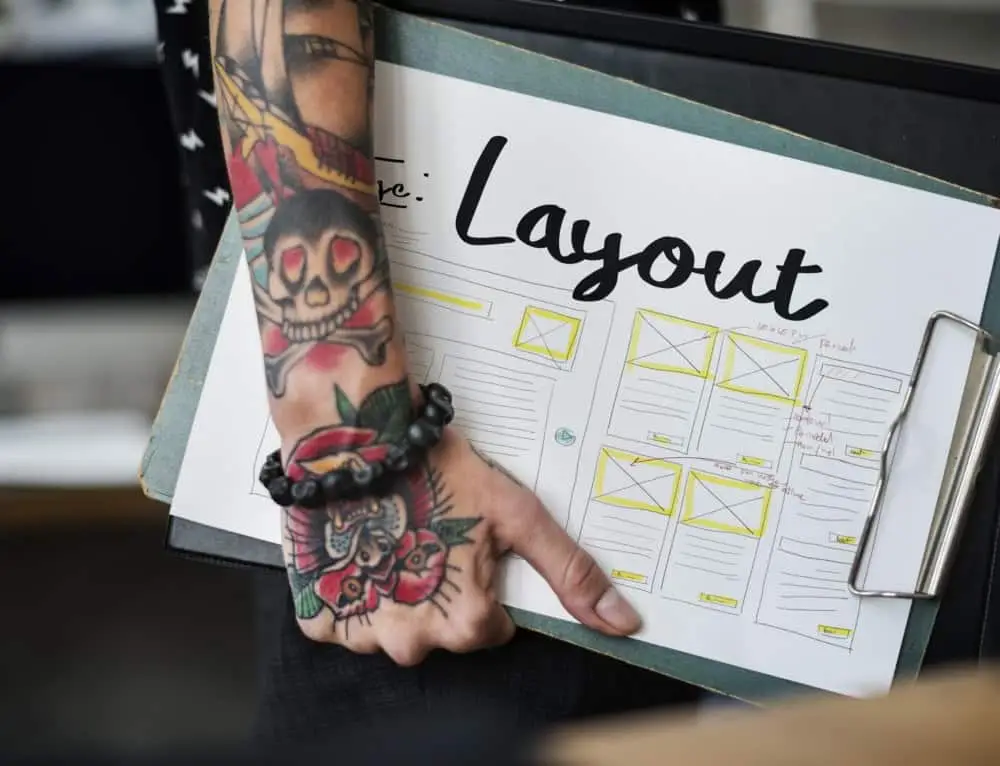 Alt: Illustration eines Website-Layouts auf Papier, bei einem Designer mit Tätowierungen am Arm.